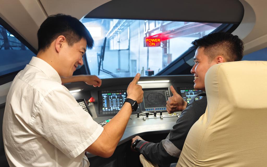 8月25日，在印度尼西亞萬隆的雅萬高鐵德卡魯爾動車所內(nèi)，中國師傅穆振（左）在向印尼火車司機塞蒂亞萬講解動車組出庫前的上電作業(yè)。